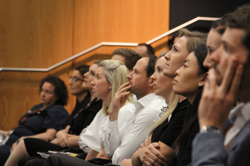 Group of people sitting in lecture theatre focused on someone presenting to them out of shot.