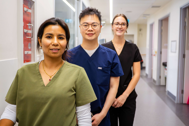 Three healthcare workers stand shoulder-to-shoulder in a hospital ward.