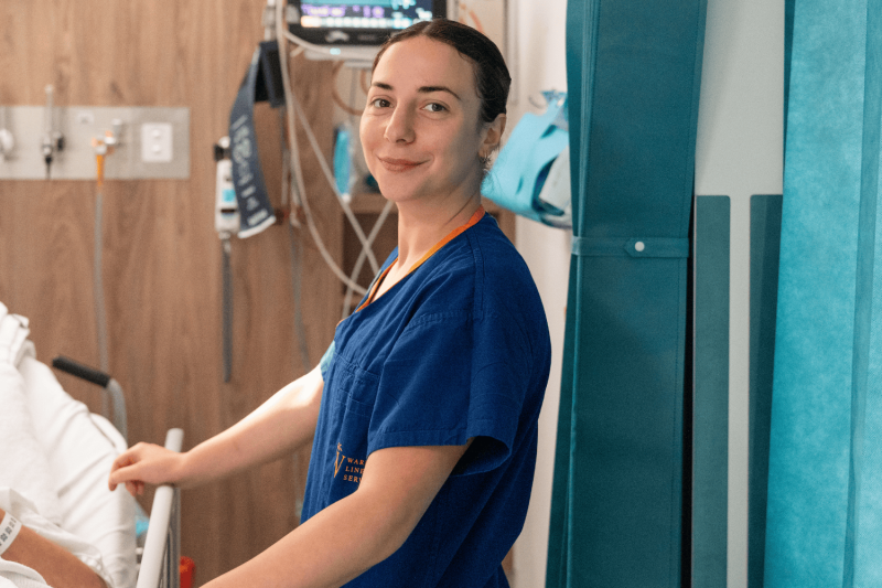 Female nurse smiling at camera by patient bedside