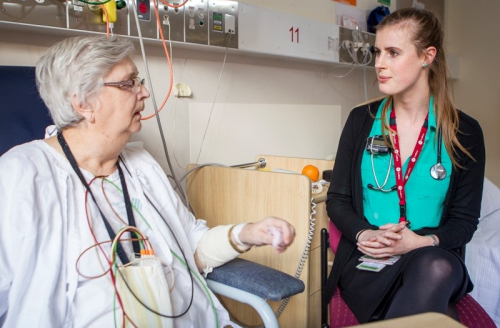Patient wearing cardiac monitoring sitting in chair with doctor talking to her