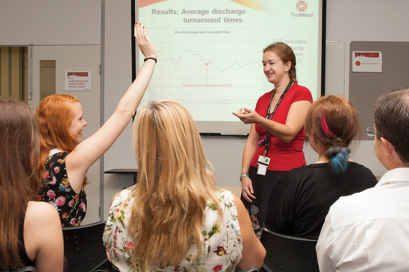 Photo from the audience at a pharmacy lecture with one pharmacist raiding her hand to ask a question of the speaker