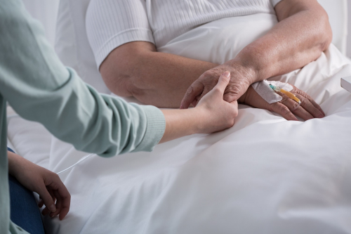 Patient in bed with IV cannula in her hand and the other hand is holding the hand of a caring woman whilst they chat