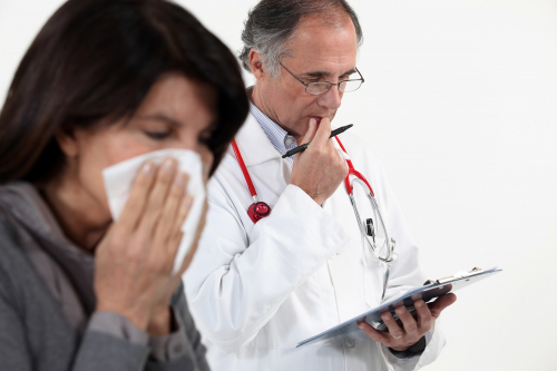 Doctor looking at a clipboard whilst patient is sneezing with a hanky