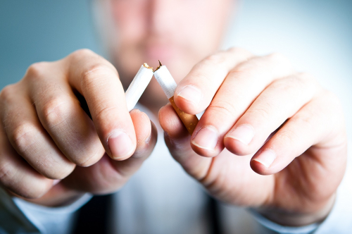 Man breaking a cigarette, hands in focus snapping cigarette, face blurred in the background