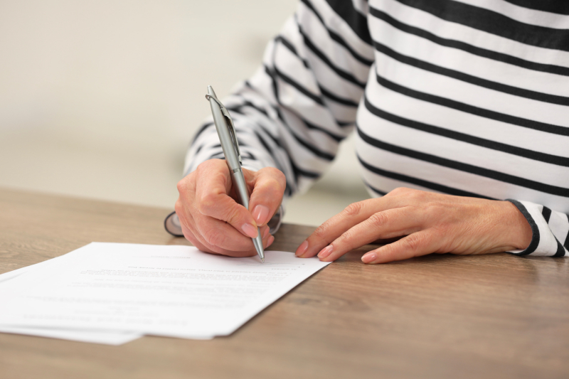 Woman signing Last Will and Testament at wooden table.